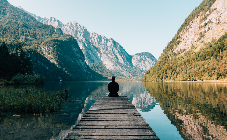 Man sitting on a dock in front of a beautiful vista of a lake and mountains