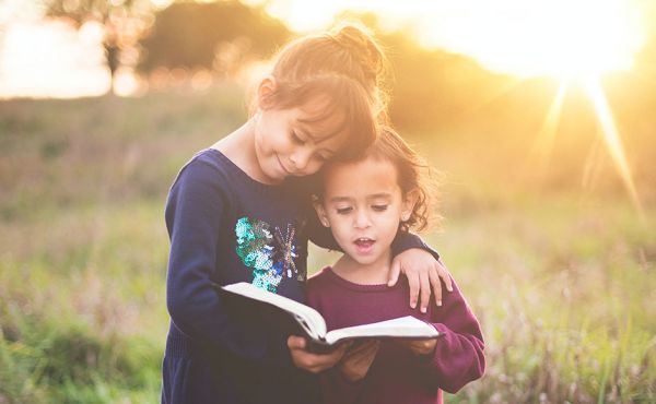 Two girls reading bible in a field