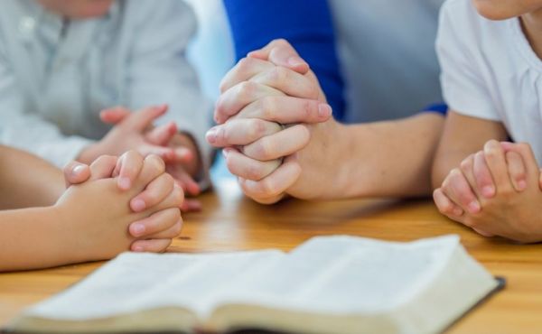 Family's hands praying around a table