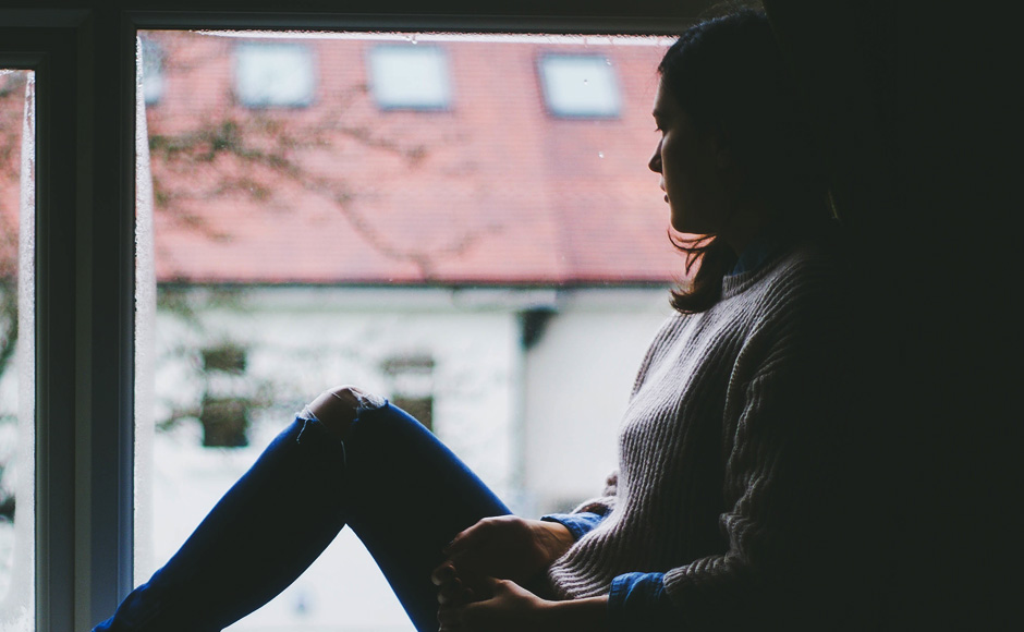 The shiloutte of a woman stares out of a window