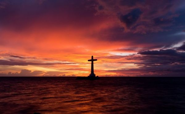 Cross standing out at sea at sunset 