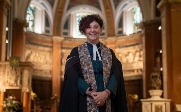 Rev Sally Foster-Fulton wearing her robes and smiling inside St Cuthbert's Church in Edinburgh.